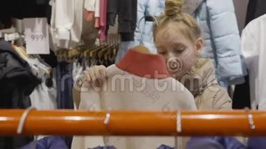 年轻的少女在购物时在服装陈列室里看夹克。 年轻女子在时装精品店挑选服装